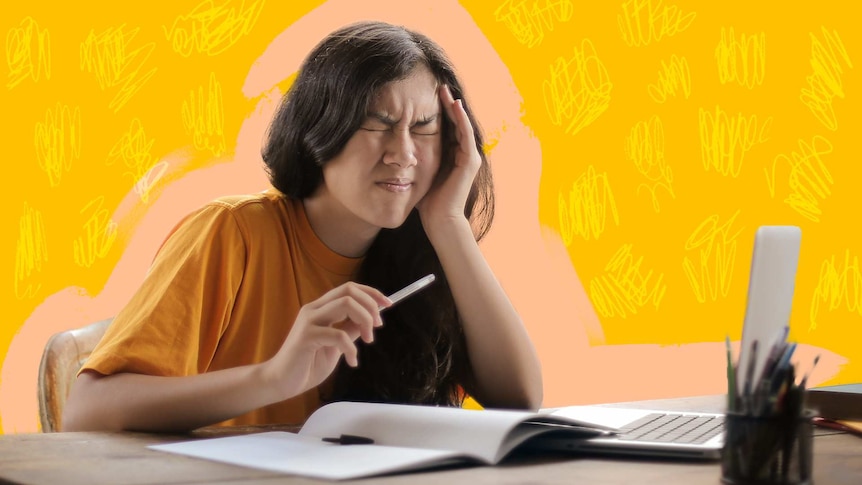 Woman holds her head in her hands while sitting at a workspace, in a story about managing 'COVID brain' while working from home.