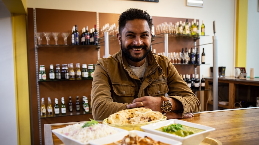 Indian man smiling with bowls of curry and rice