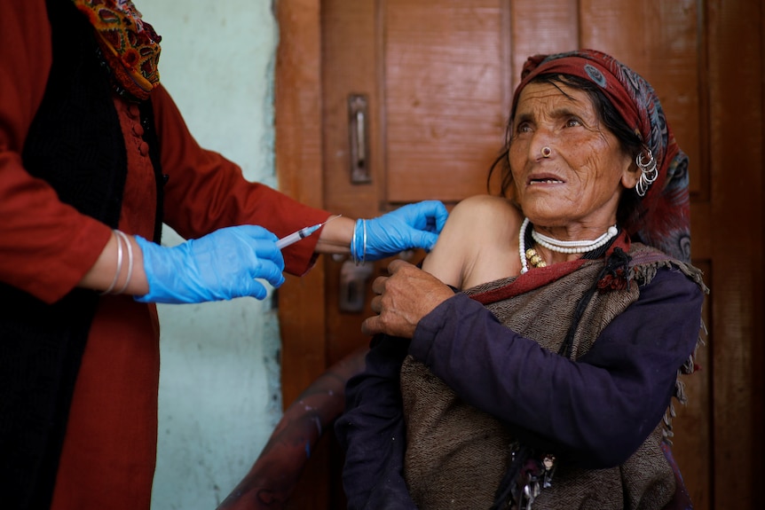 An Indian woman holds down her sleeve as the hands of a health worker wearing blue gloves administers her vaccine.