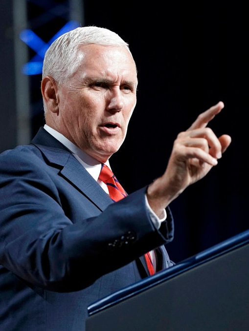 Mike Pence stands at a podium wearing a blue suit and red striped tie, gesturing as he speaks