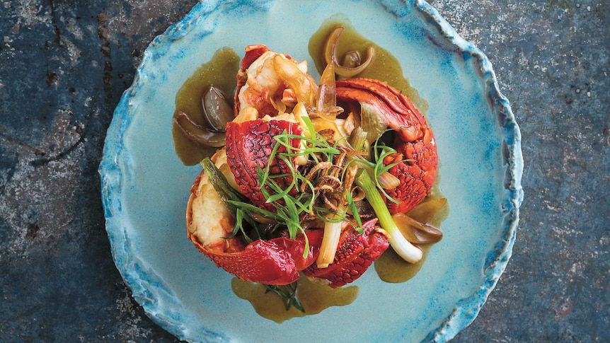 Cantonese stir-fried lobster delicately arranged on blue shell plate with smaller bowl of fried shallots.