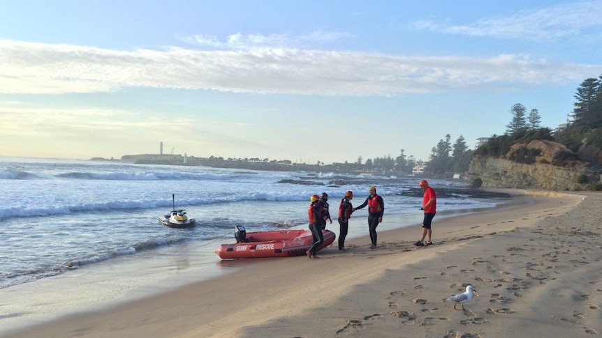 A jet ski in the water and surf live savers dragging a red rescue inflatable boat onto the beach.