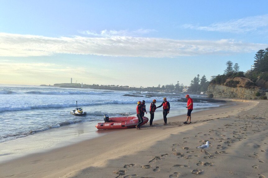 A jet ski in the water and surf live savers dragging a red rescue inflatable boat onto the beach.