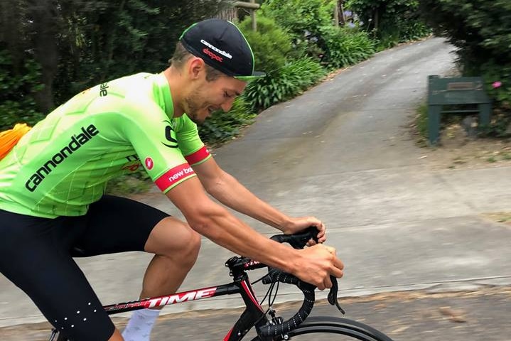 Damion Drapac smiles as he cycles uphill in a fluoro green outfit.