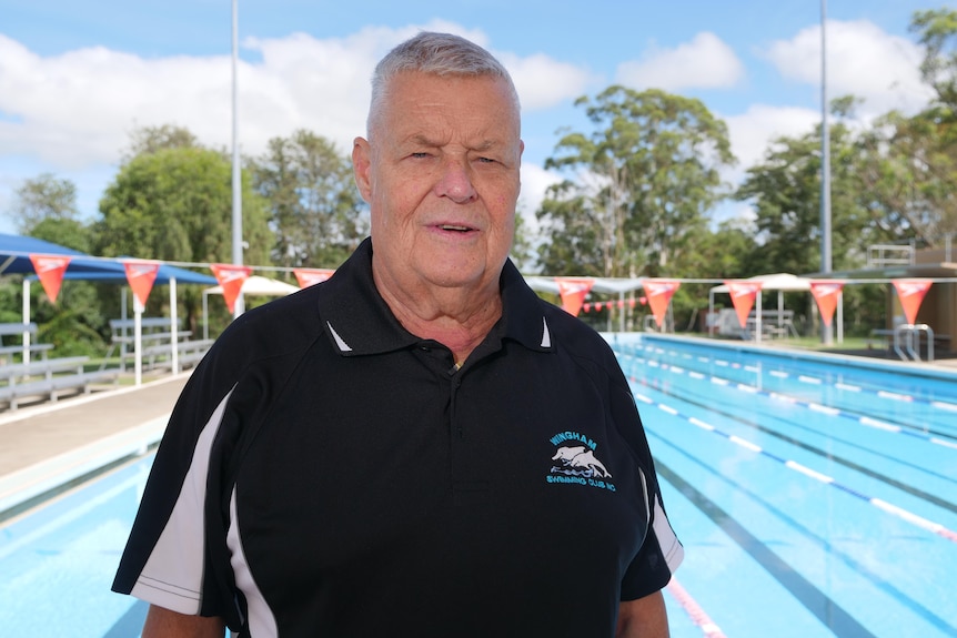 A man stands in front of a public swimming pool.