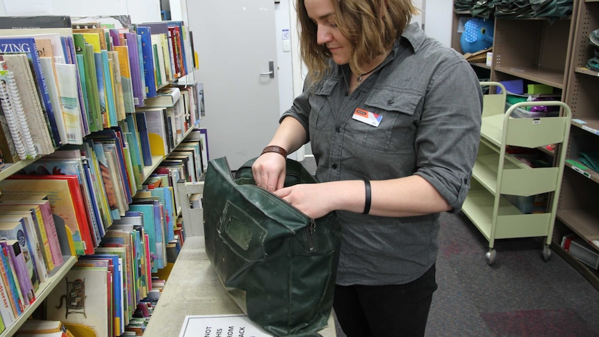 A woman is surrounded by an isle of books while she packs a green library bag