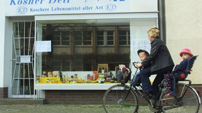 A woman rides her bike past a kosher food store in central Berlin, Germany