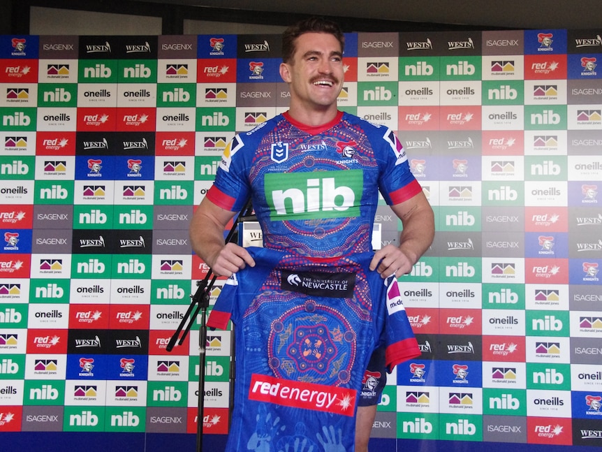 Football player holding up playing jersey with Indigenous design.