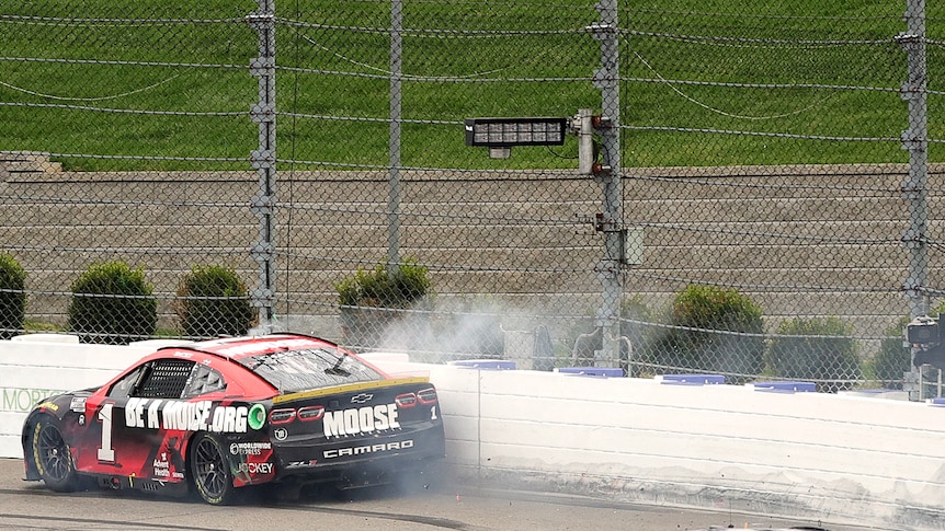 A racing car skids along the wall of a racetrack with smoke coming out during a race