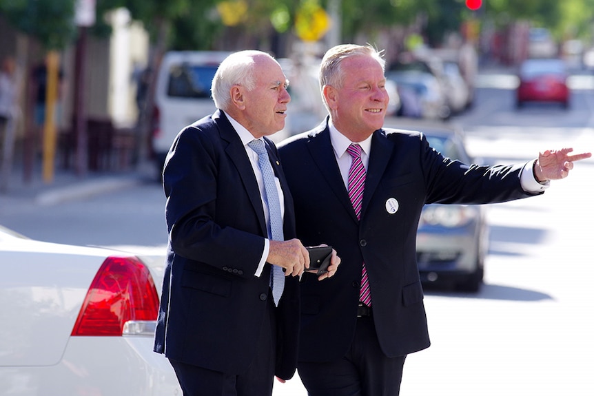 Colin Barnett on a street  points to something, John Howard leans in to look.