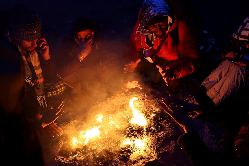 Men huddle around a fire warming their hands in the night.