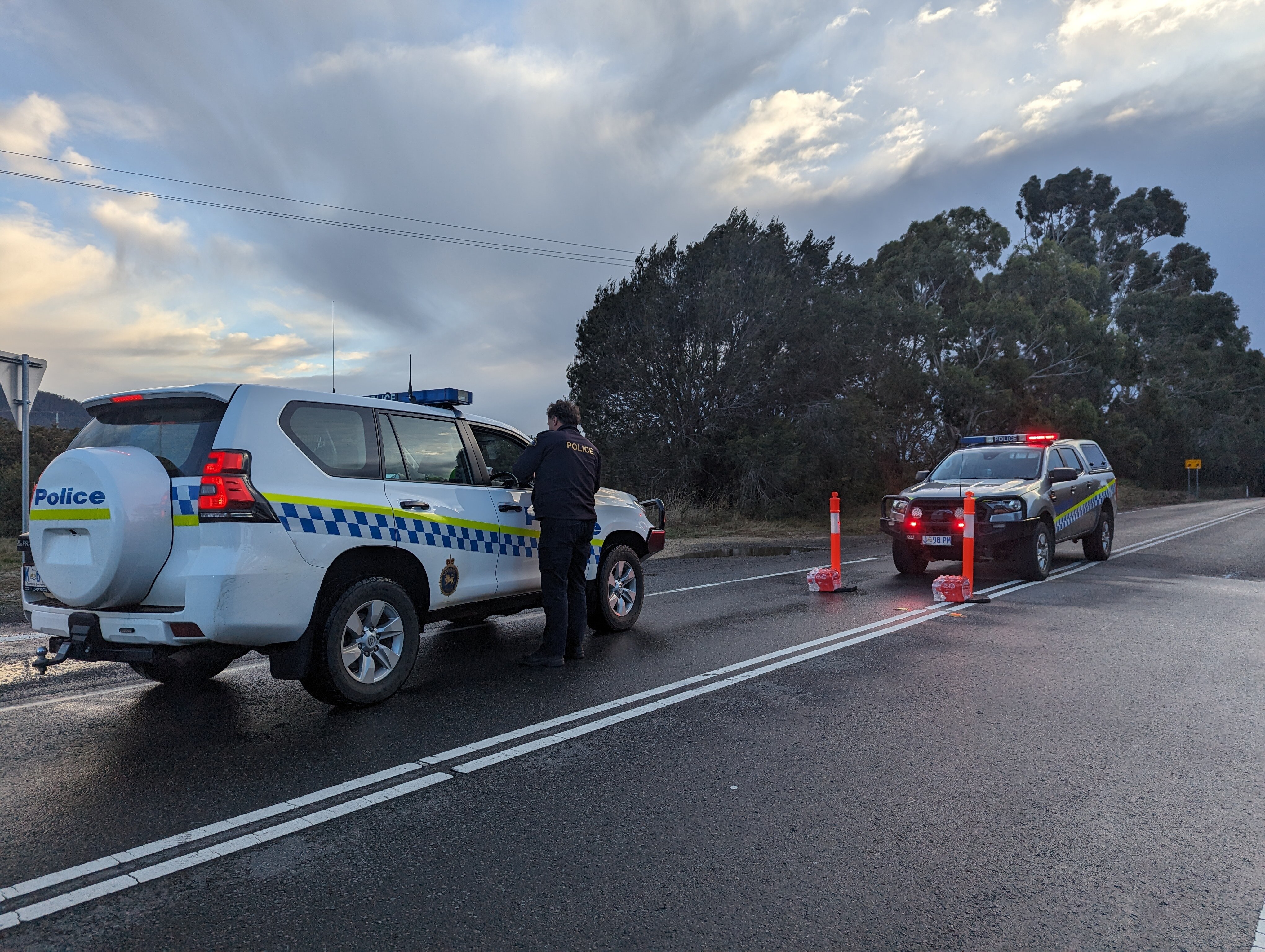 Two police cars stopped facing each other in the middle of a road with an officer standing at the window of one.