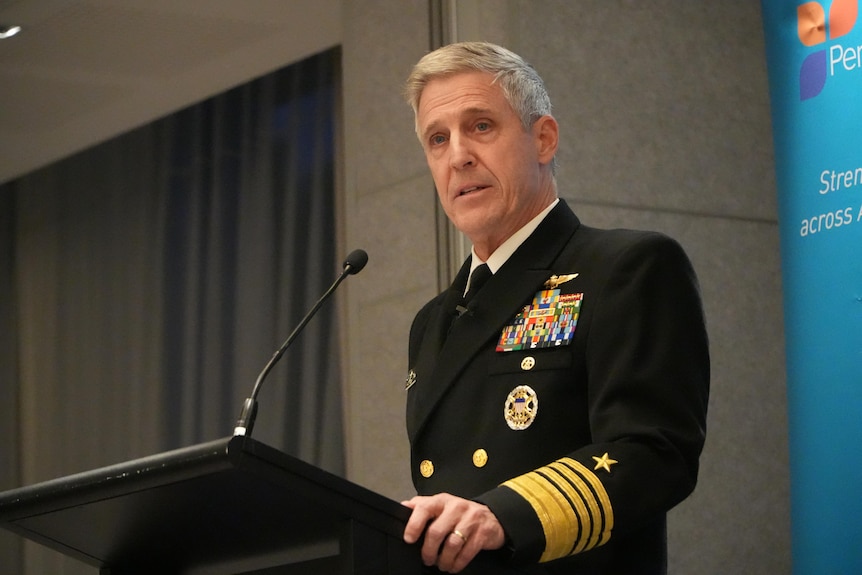 A man named Admiral Stephen Koehler speaks at a lectern while wearing full dress military uniform.