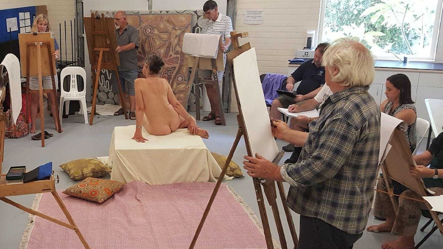 Life drawing class watching Nude Model Jo Ernst sitting in the middle of the room.