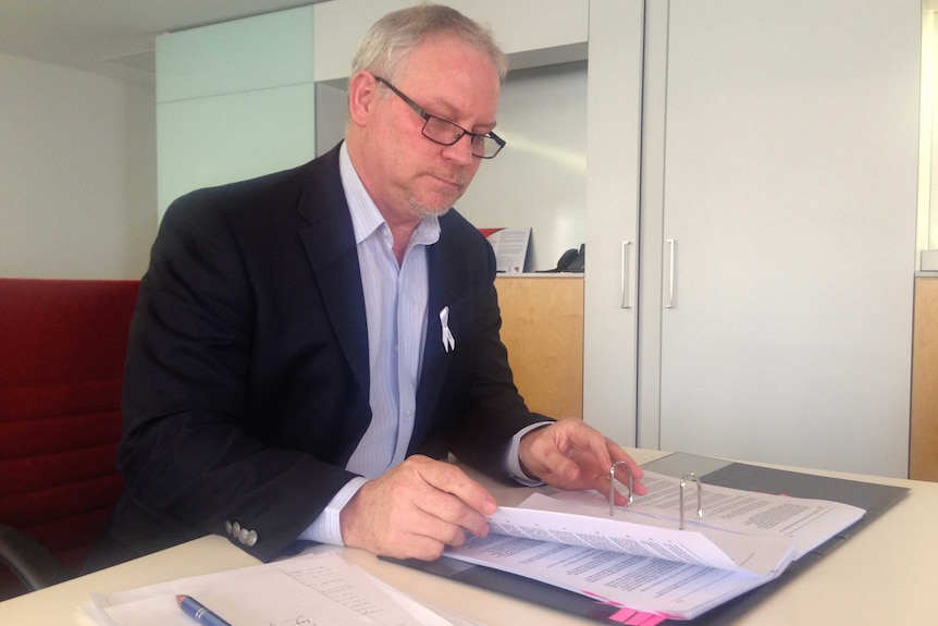 A middle-aged man looking at a file on his desk