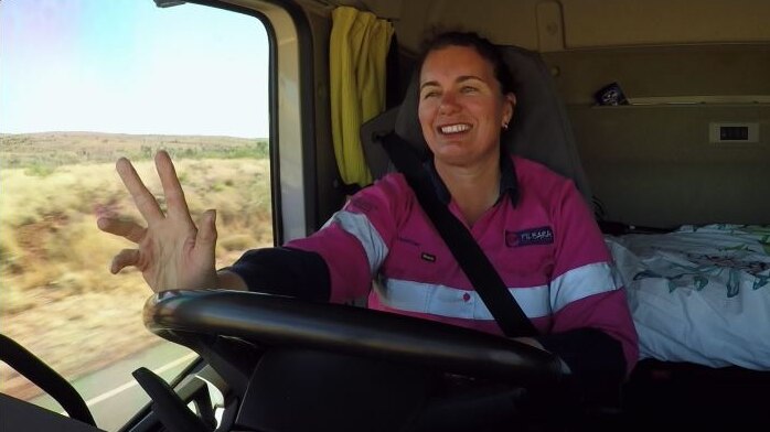 A female driver signals the 'trucky wave' to an oncoming driver from her seat.