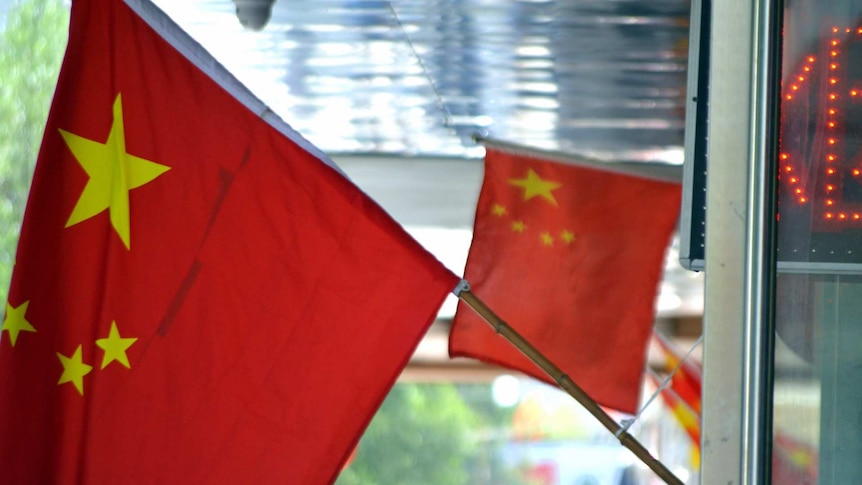 Two flags of the People's Republic of China hang outside a shopfront in Asia.