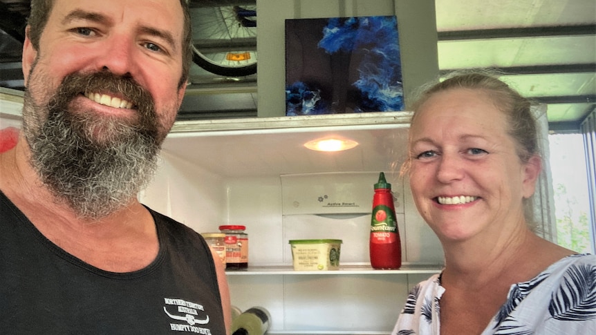 Man and woman smiling in front of empty fridge.