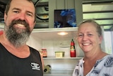 Man and woman smiling in front of empty fridge.