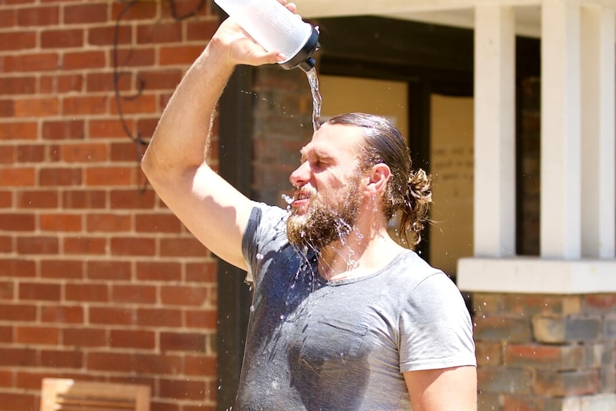 A picture of a man pouring water over himself from a water bottle