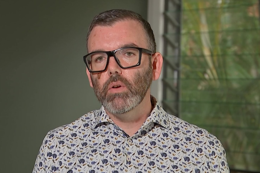 A man in glasses with a large brown mark on one cheek