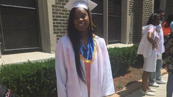 Akyra Murray wearing a pink graduation gown and cap and smiling for the camera