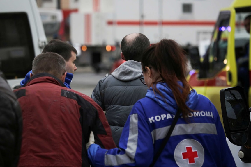 A paramedic leads an injured person through a crowd