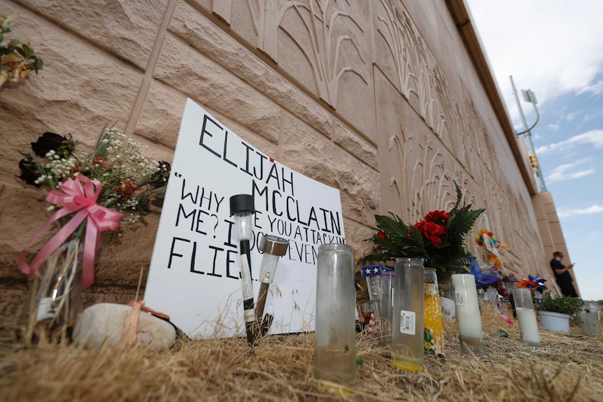 A wall is lined with flowers, signs and a cross.