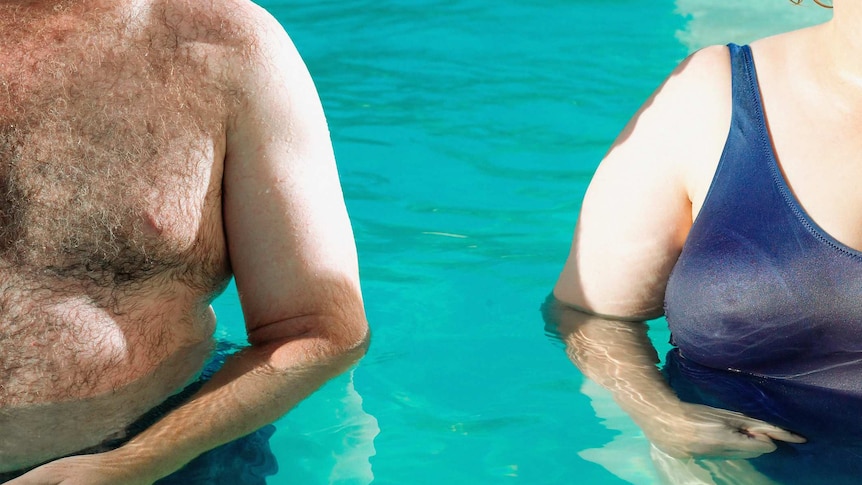 Unidentified overweight man and woman stand shoulder to shoulder in swimming pool.
