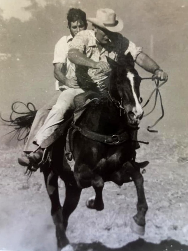 Black and white photo of two men riding a horse at full gallop.