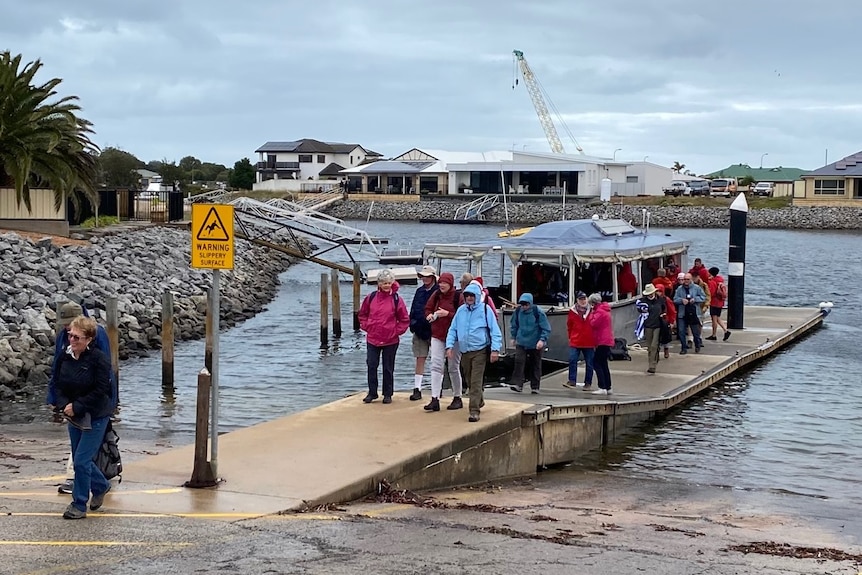 Group of people walking along boat ramp after disembarking from boat in marina, houses in background