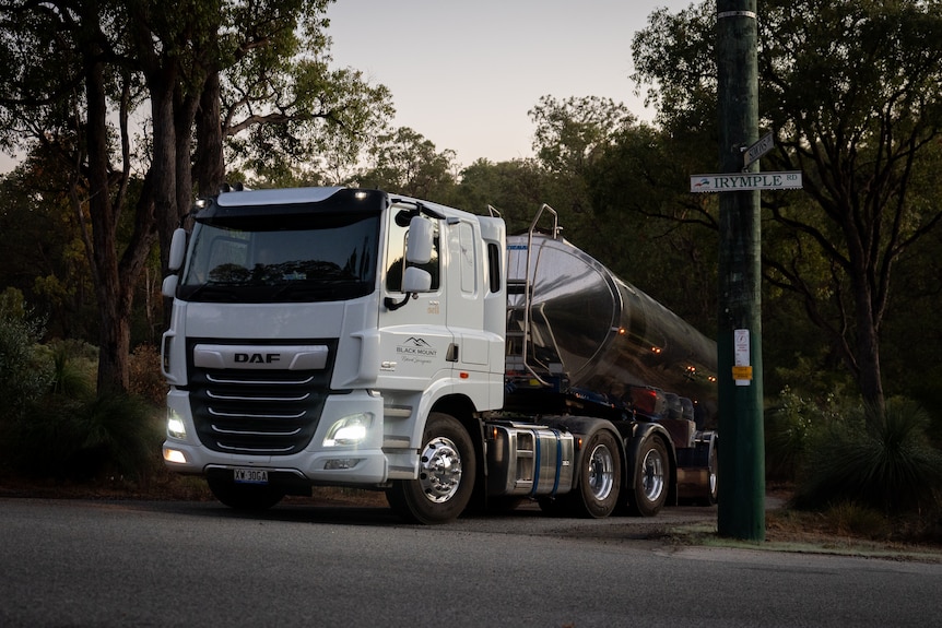 A large truck with a silver tank driving out of a rural property.
