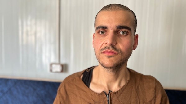 A gaunt man in brown prison garb stares straight ahead at the camera
