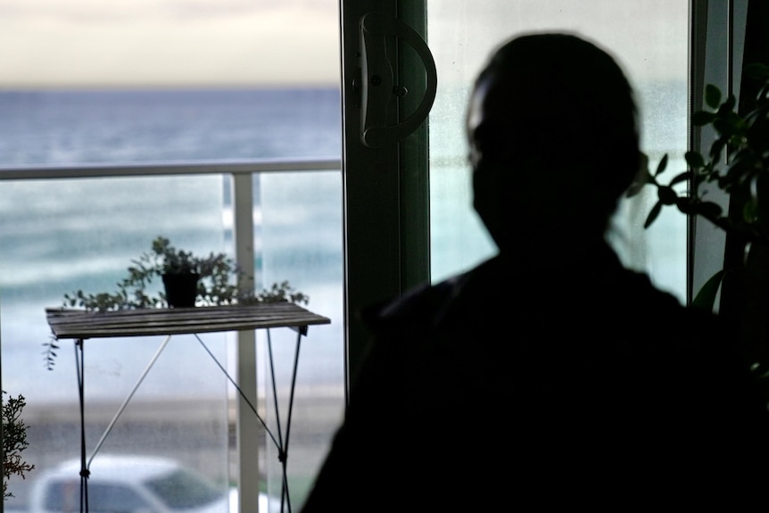 A woman sits in the shadow in a room.