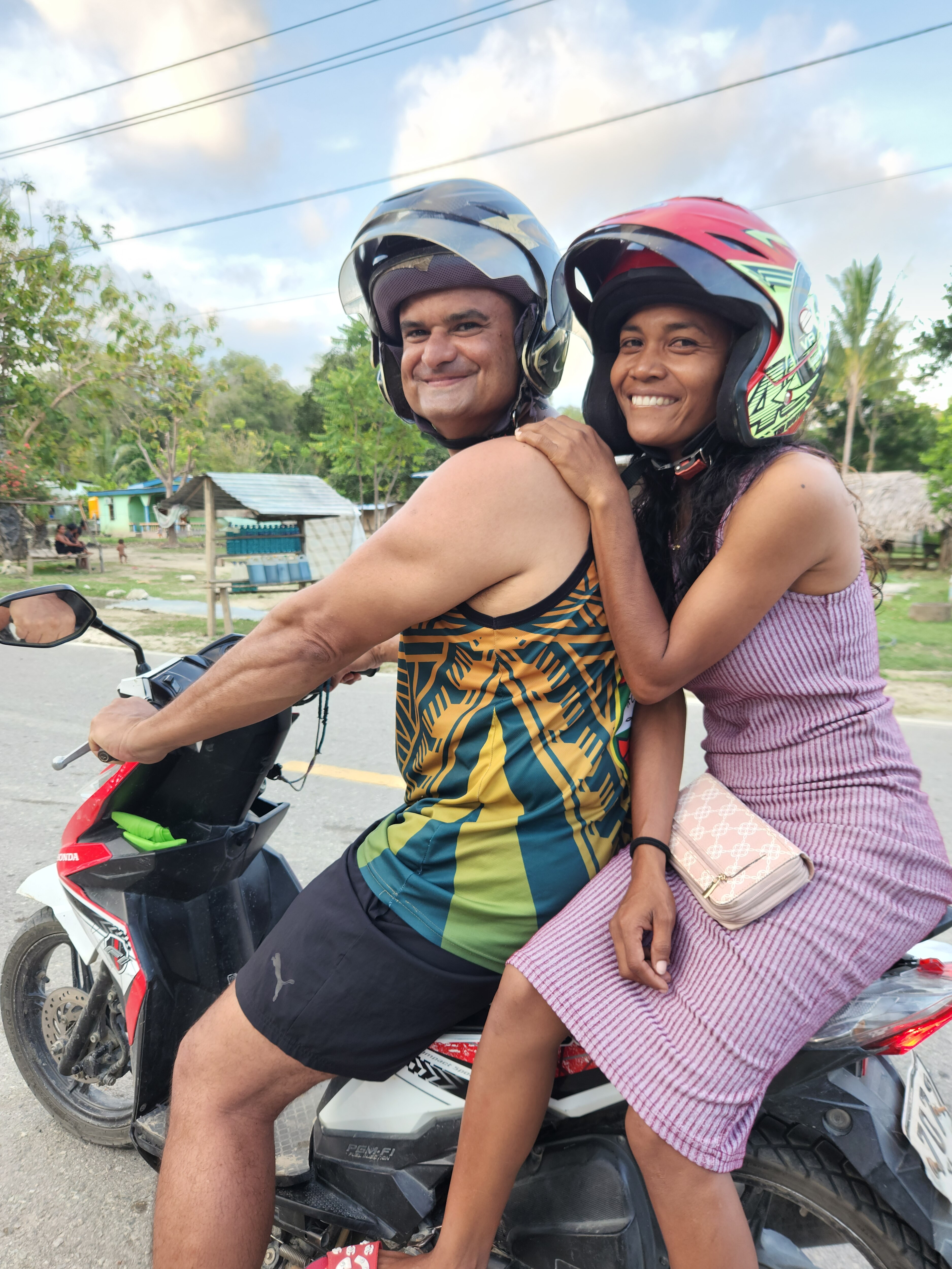 Michael and Bella sit on a motor-scooter and smile. 