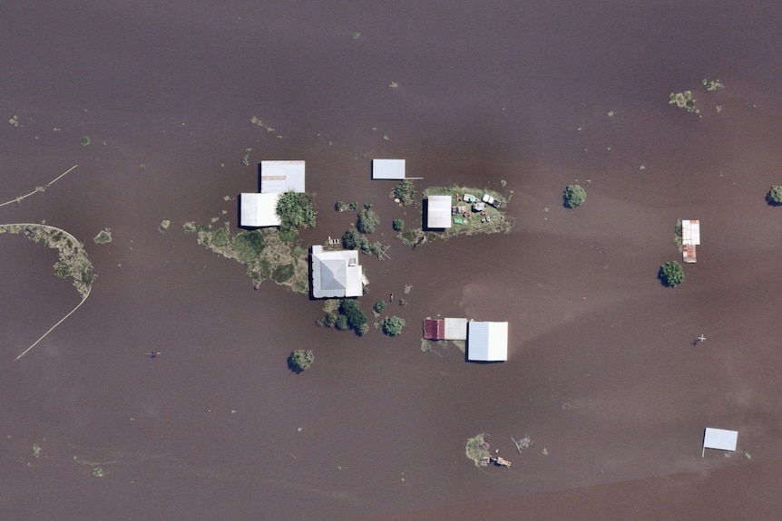 A farmhouse and outbuildings are almost completely submerged by floodwaters, as seen from above.