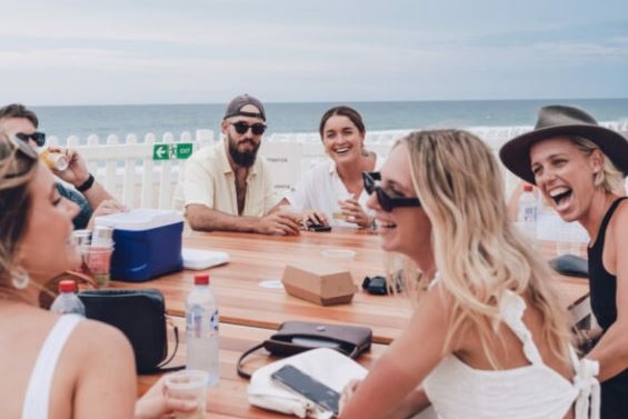 People aged in the 20 & 30s socialising at a beach bar table.