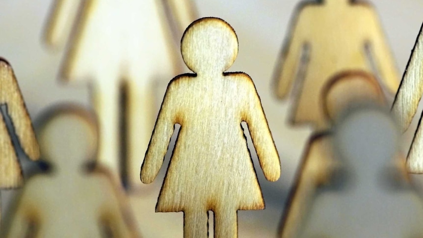 Wood cut-out female silhouettes standing together on a beige background.