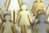 Wood cut-out female silhouettes standing together on a beige background.
