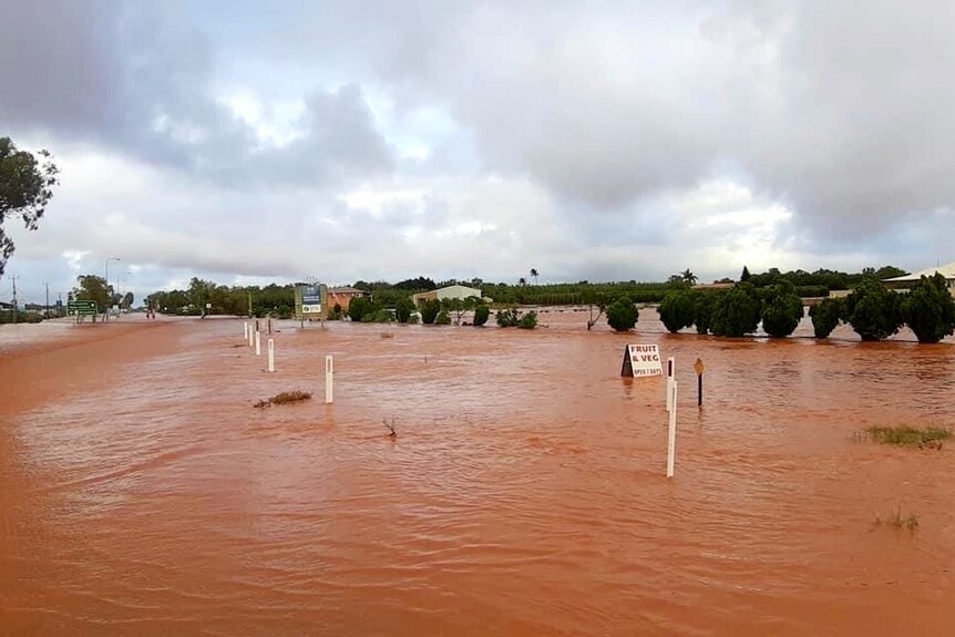 A wide view of road markers, bushes and buildings standing in reddish-brown water that stretch into the distance.