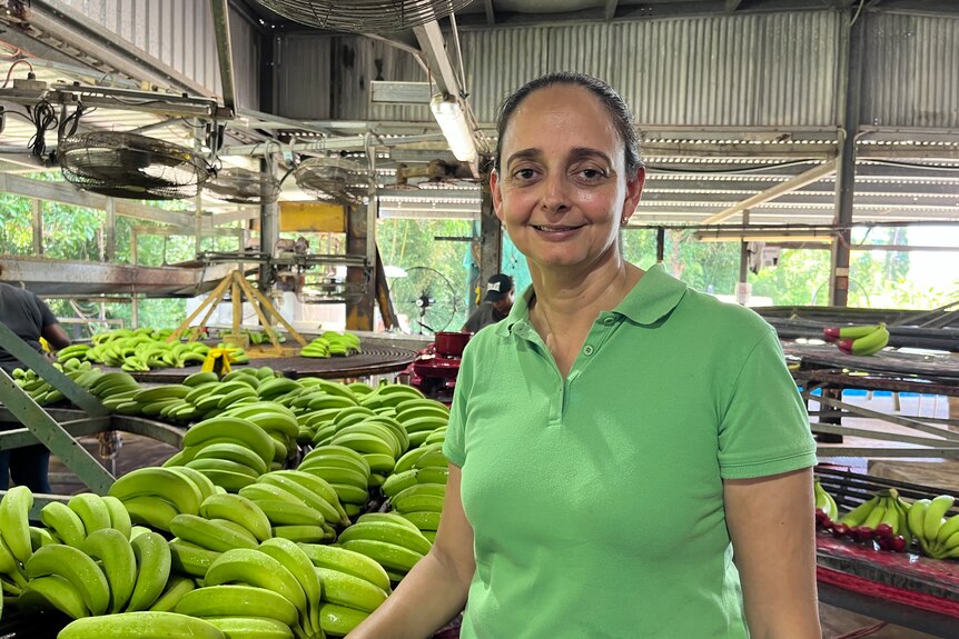 Woman smiles at camera wearing green shirt standing in her banana packing shed