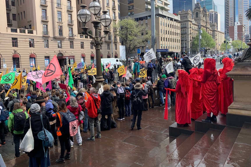 A group of protestors hold flags with the extinction rebellion symbol and stand in the street with police nearby.