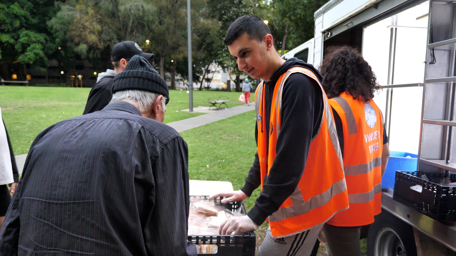 A young man standing by a fold-out table speaks to an elderly man