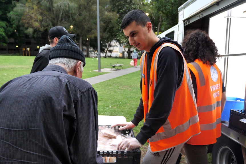 A young man standing by a fold-out table speaks to an elderly man