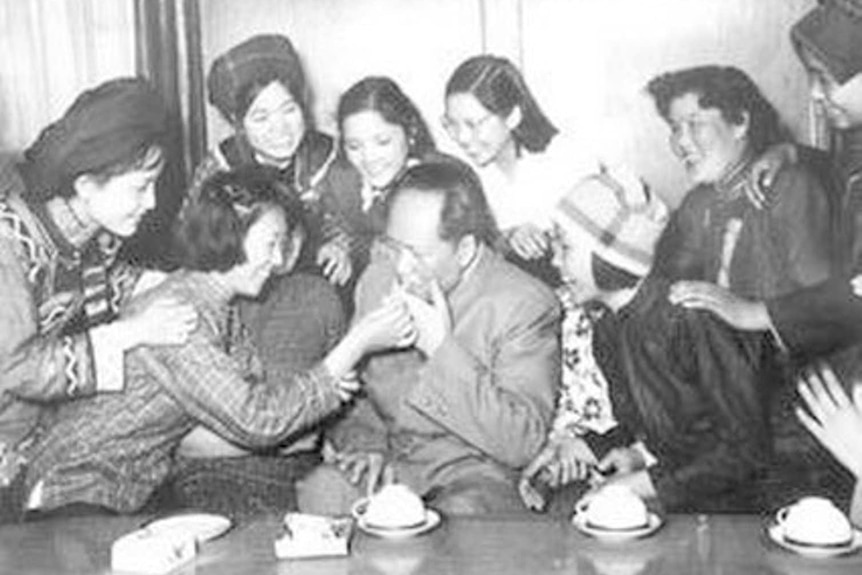 A black and white photo of Mao Zedong sitting at a table surrounded by Chinese women