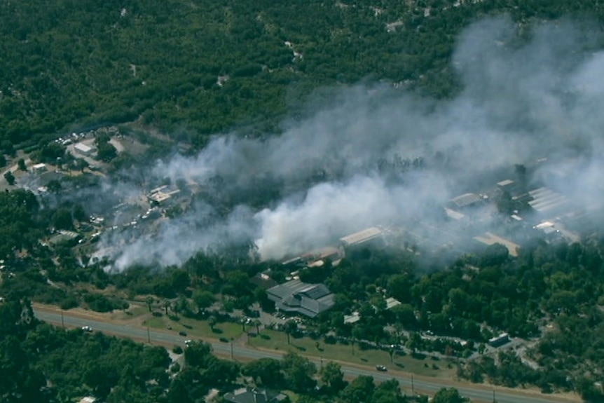 Smoke billows from dense bushland in a semi-rural neighbourhood