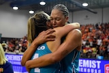 Two women's basketballers embrace on court after a game.  