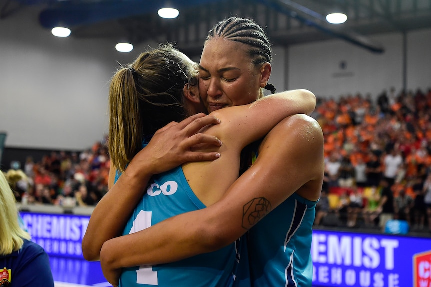 Two women's basketballers embrace on court after a game.  