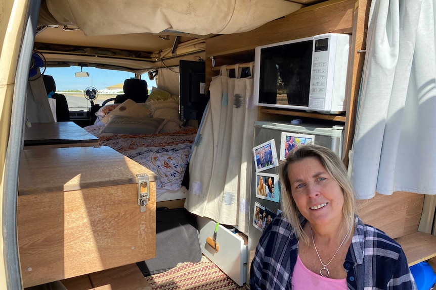 woman sittin gon the edge of a campervan. behind her is a fridge with photos on the door, microwave