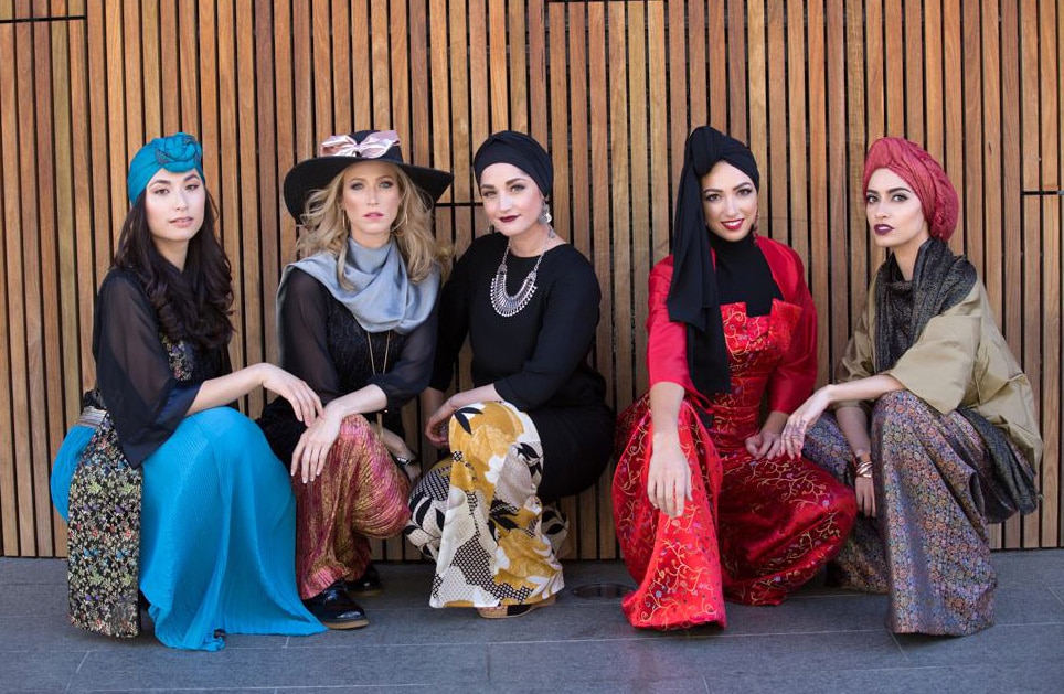 Five models wearing modest fashions crouched down in a line.